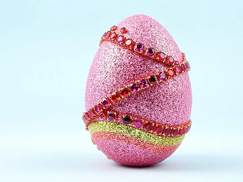 Pink glitter egg encrusted with pink ruby garnets, with spiral bands of Garnetts wrapped around in a helix with colors arranged as rainbow stripes