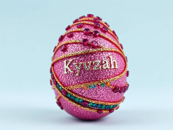 Pink glitter egg encrusted with pink ruby garnets, with spiral bands of garnetts wrapped around in a helix with colors arranged as rainbow stripes, with the name Kyzah painted on the egg
